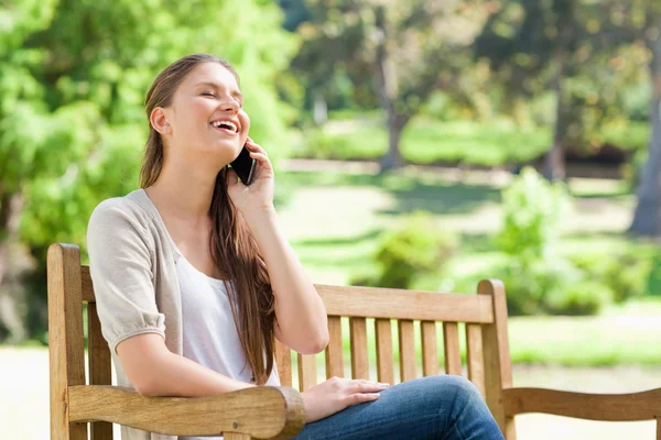 在公园的长凳上，她的手机上笑的女人 — 图库照片