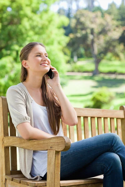 Gülümseyen kadın cep telefonunu bir parkta bankta oturuyor — Stok fotoğraf