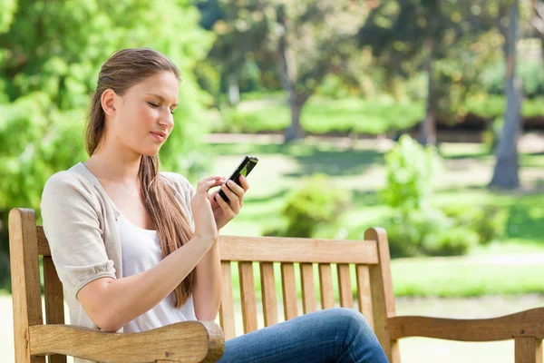 Woman writing a text message on her cellphone while on a park be — Stock Photo, Image