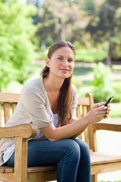 Женщина со своим телефоном сидит на скамейке в парке — стоковое фото