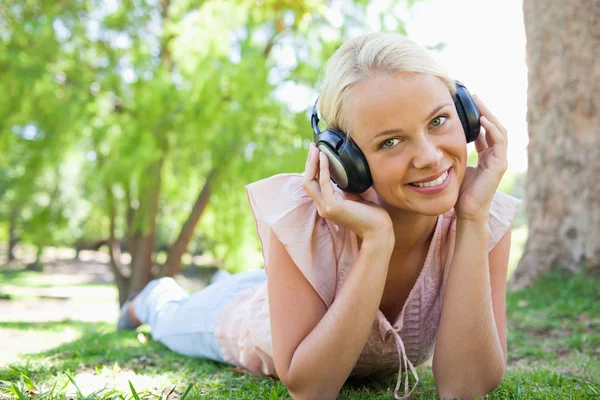 Mujer sonriente escuchando música mientras está acostada en el césped —  Fotos de Stock
