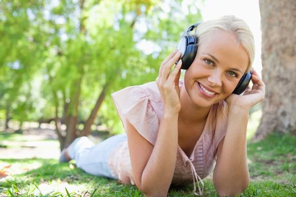 Uśmiechnięta kobieta, leżąc na trawie słuchając muzyki — Zdjęcie stockowe