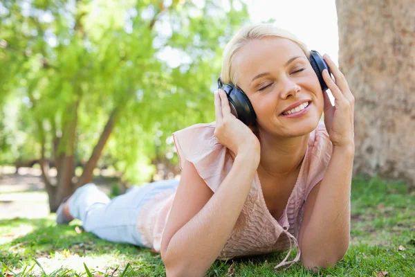 Woman wearing headphones while lying on the lawn — Stock Photo, Image