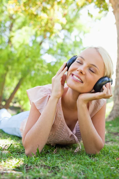 잔디밭에서 음악을 즐기는 헤드폰으로 웃는 여자 — 스톡 사진