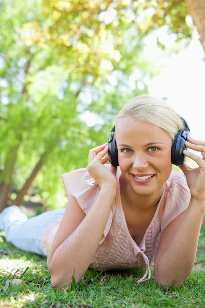 Улыбающаяся женщина в наушниках наслаждается музыкой на траве — стоковое фото