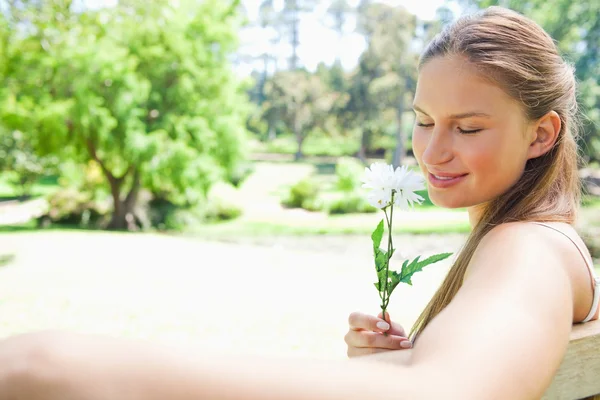 Side view of a woman on a park bench smelling a flower — Stock Photo, Image