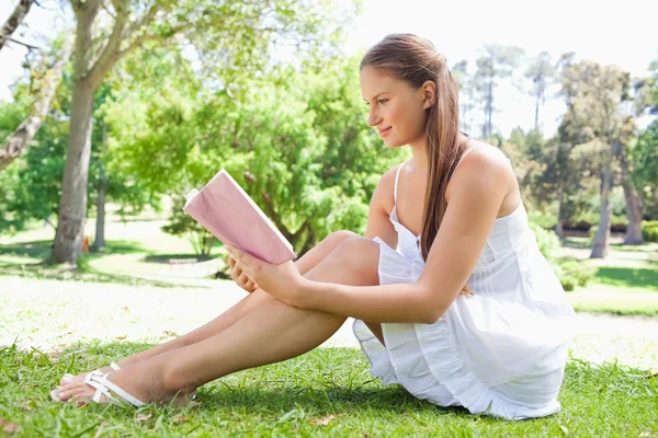 Vista lateral de una mujer sentada en el césped mientras lee un libro —  Fotos de Stock