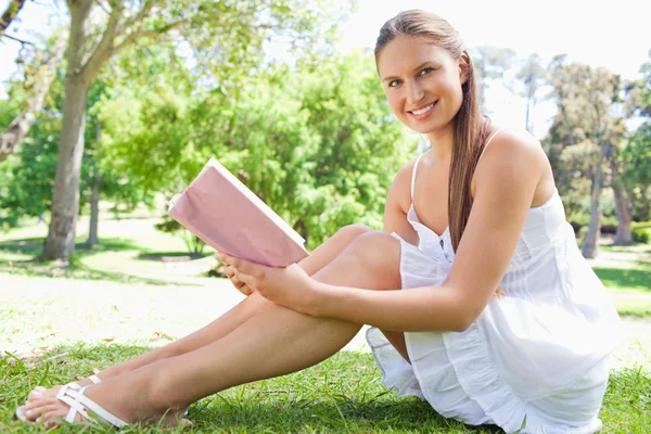 Вид сбоку улыбающейся женщины, сидящей на лавке с книгой — стоковое фото
