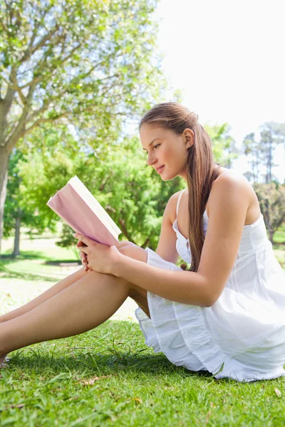 Vista lateral de una mujer leyendo un libro sobre la hierba —  Fotos de Stock