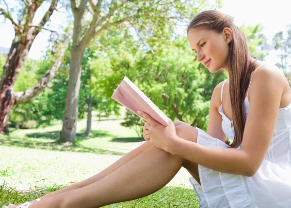 Vedere laterală a unei femei care stă pe peluză în timp ce citește o carte — Fotografie, imagine de stoc
