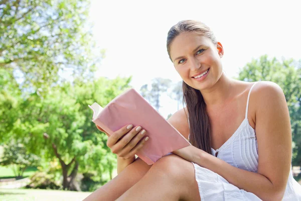 Vista lateral de una mujer sonriente con una novela en el parque —  Fotos de Stock