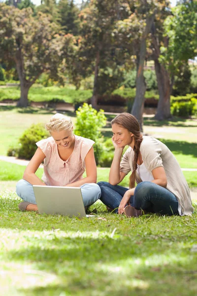 Улыбающиеся друзья с ноутбуком, сидящим на газоне — стоковое фото