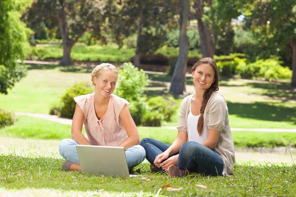 Mujeres sonrientes sentadas en el parque con un portátil — Foto de Stock