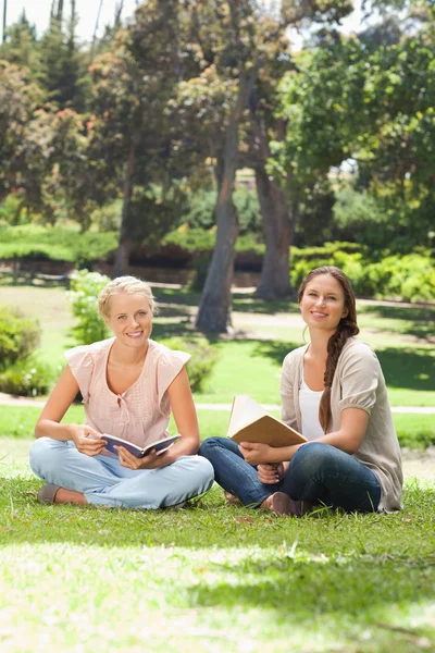 Mujeres sonrientes con sus libros sentadas en el parque — Foto de Stock