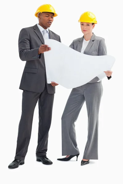 Geschäftsmann und Frau mit harten Hüten, die Papier halten — Stockfoto