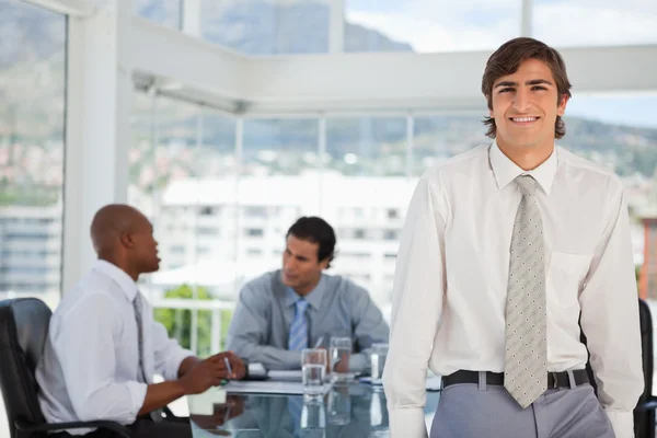 Smiling young businessman leans on table — Stock Photo, Image