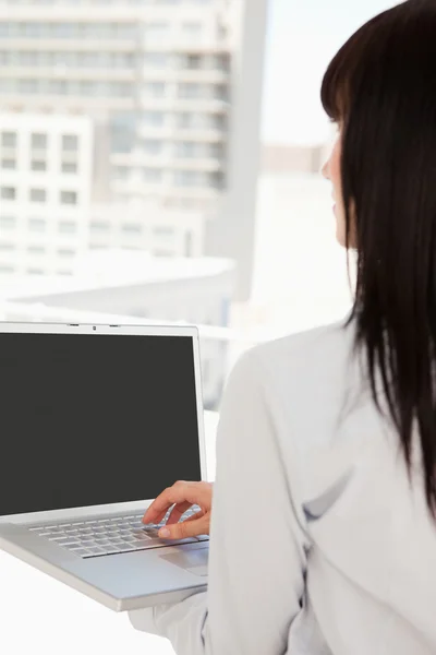Vrouw met behulp van haar laptop terwijl u uitkijkt op het venster — Stockfoto