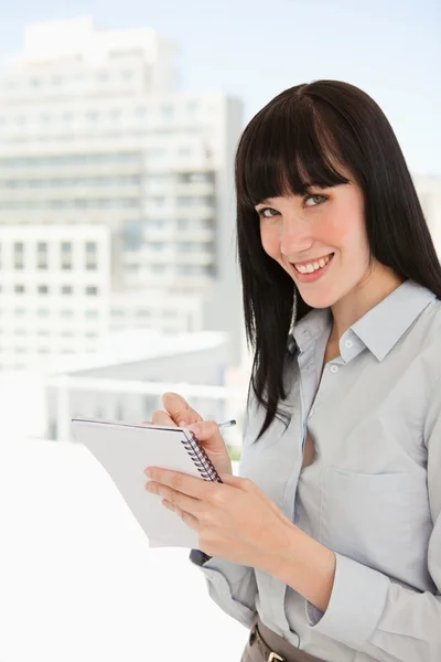 A smiling woman with a note pad and pen looking into the camera — Stock Photo, Image