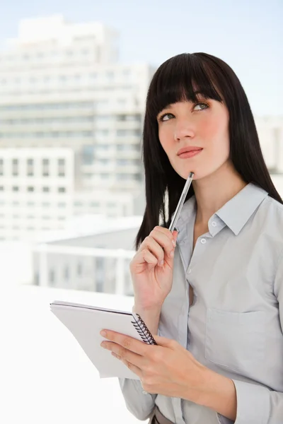 Eine denkende Frau in ihrem Büro blickt nach oben, während sie einen Zettel in der Hand hält — Stockfoto