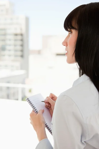 Une femme avec un bloc-notes regarde vers le haut alors qu'elle cesse d'écrire — Photo