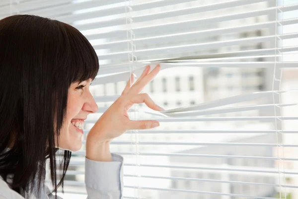 A smiling woman looks out through her blinds — Stock Photo, Image