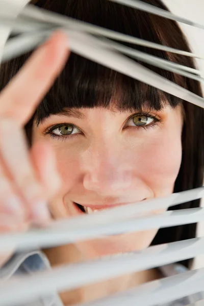 Close up van vrouw op zoek via blinds in de camera — Stockfoto