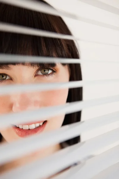 A woman looking forward through her blinds without moving them — Stock Photo, Image