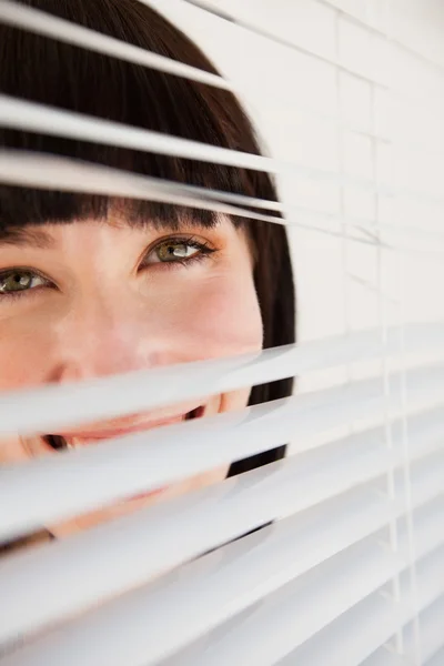 Uma mulher olhando através de persianas que ela abriu ligeiramente — Fotografia de Stock