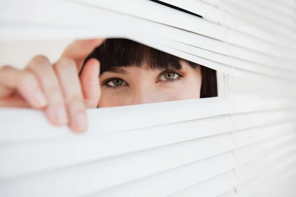 A woman opening a part of closed blinds with her fingers — Stock Photo, Image