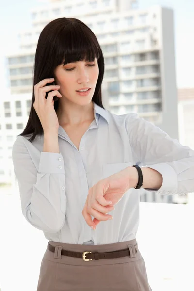 Eine Frau, die einen schnellen Anruf macht, während sie die Uhrzeit überprüft — Stockfoto