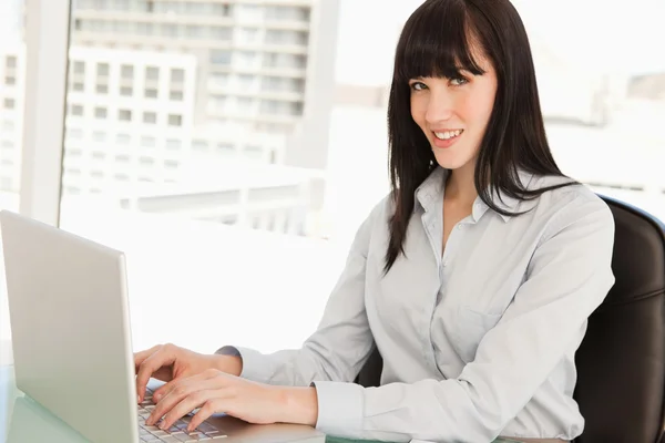 A woman looks at the camera as she types on her laptop — Stock Photo, Image
