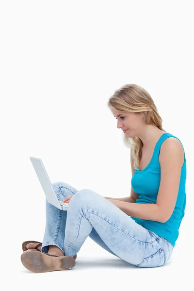 一名女子坐在地上在便携式计算机上键入的侧视图 — 图库照片