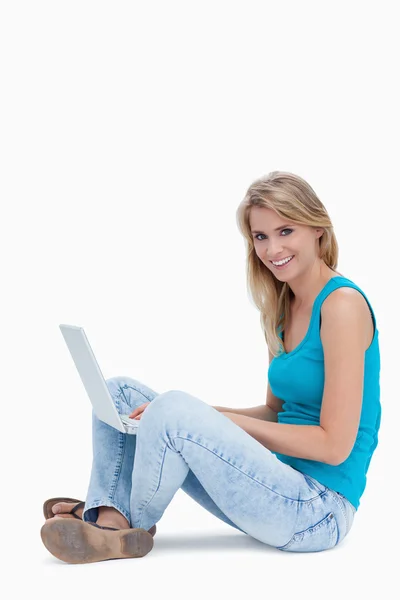 Une femme souriant à la caméra avec un ordinateur portable sur la jambe — Photo