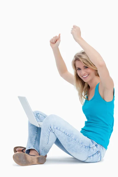 Smiling woman has her arms in the air with a laptop between her — Stock Photo, Image