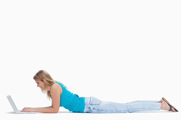 Uma mulher está deitada no chão digitando em seu laptop — Fotografia de Stock