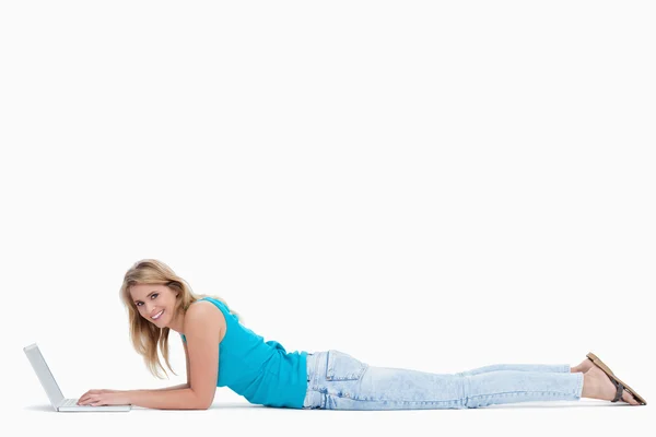 Uma mulher sorrindo para a câmera está deitada no chão digitando em h — Fotografia de Stock