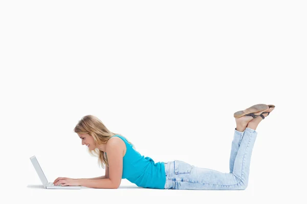 A woman lying on the floor with her legs up is typing on her lap — Stock Photo, Image