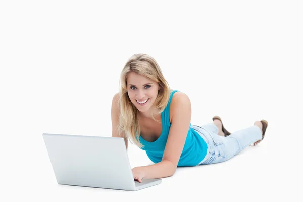Una mujer sonriente está tumbada en el suelo con una computadora portátil frente a —  Fotos de Stock