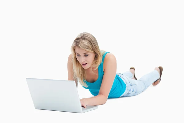 A surprised woman looking at a laptop is lying on the floor — Stock Photo, Image