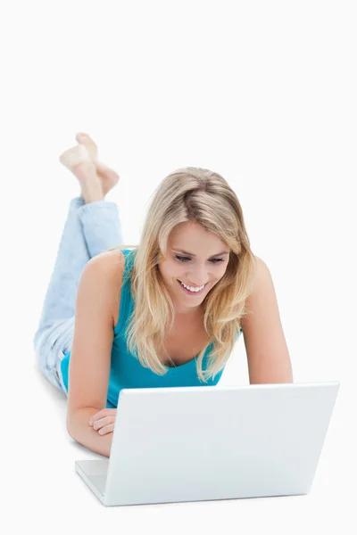 Uma mulher sorridente com um laptop está deitada no chão com sua le — Fotografia de Stock