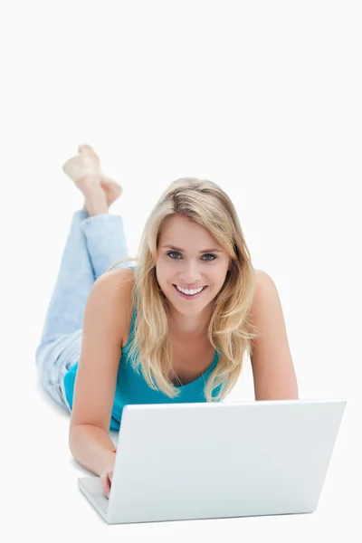 Una donna con un computer portatile è sdraiata a terra e sorride al — Foto Stock