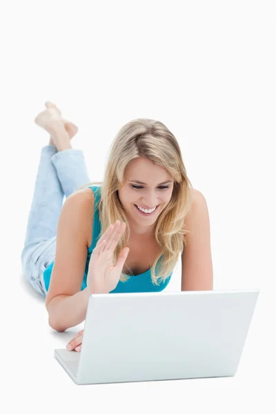 A woman with a laptop has her hand up and is lying on the floor — Stockfoto