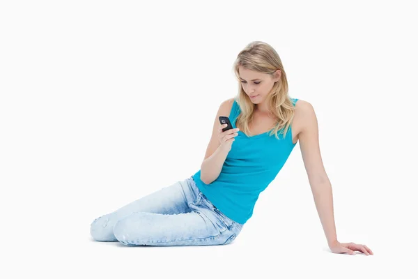 Kobieta siedzi na podłodze patrząc na jej telefon komórkowy — Zdjęcie stockowe