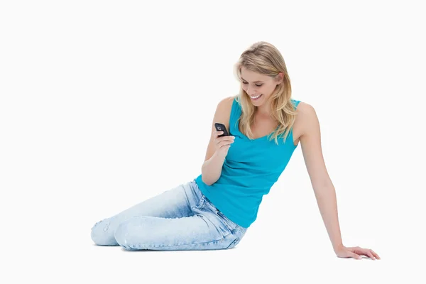 A smiling woman is sitting on the floor holding her mobile phone — Stok fotoğraf