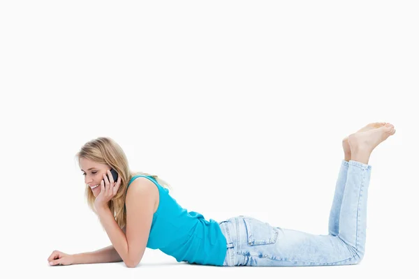 Eine junge Frau telefoniert auf ihrem Handy, während sie auf dem Boden liegt — Stockfoto