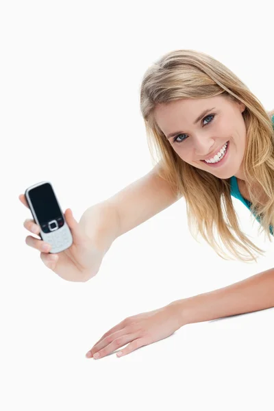A young woman holding out her mobile phone is looking at the cam — Stock Photo, Image