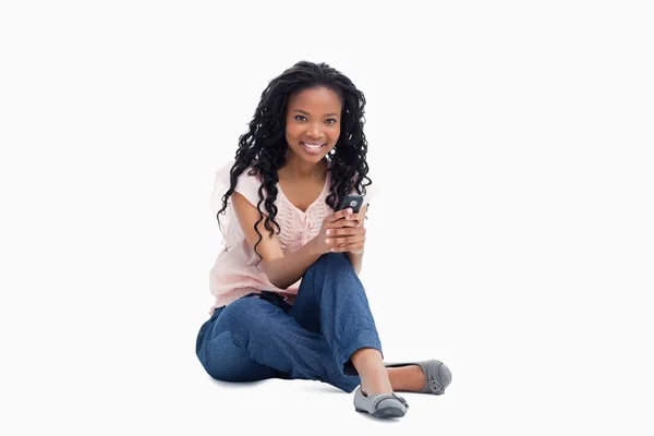 En leende kvinna som sitter på golvet håller en mobiltelefon — Stockfoto