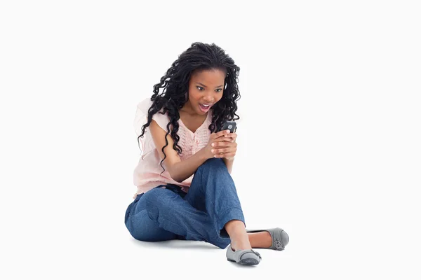 Μια έκπληξη γυναίκα κάθεται στο πάτωμα της κοιτάζοντας της κινητής τηλεφωνίας — Φωτογραφία Αρχείου