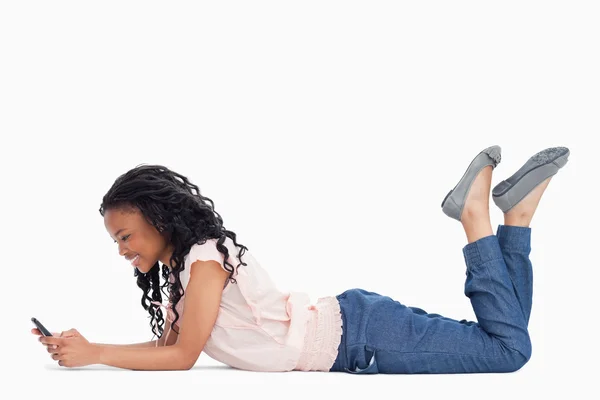 Eine junge Frau, die auf dem Boden liegt, sendet eine SMS von ihrem Handy — Stockfoto