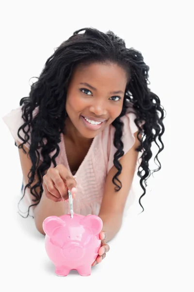 En ung flicka tittar på kameran satsar pengar på en piggy — Stockfoto